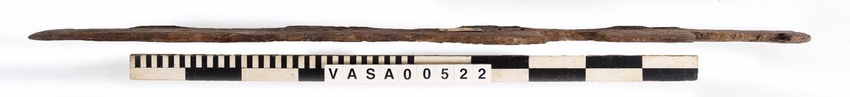 Bräda med två urtag och fem genomträngande spikhål, varav ett löper diagonalt genom ett hörn.
Mycket vittrad mot en kant. Järnlämningar kring spikhål. Avbruten i ett urtag.