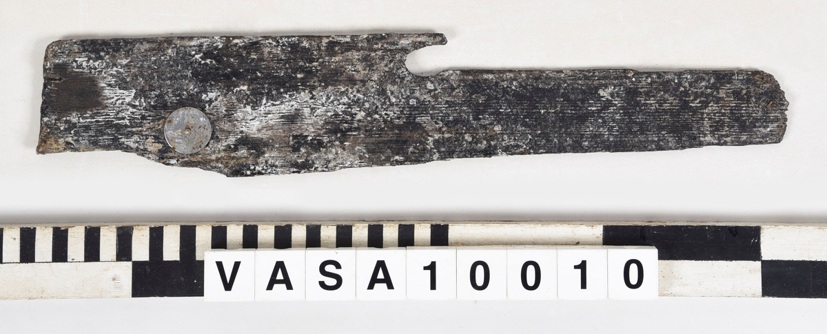 Fragment, med del av fasad kant. Ett vinklat hörn.
Mycket vittrad, smalnar av mot änden. Tjockt lager PEG.