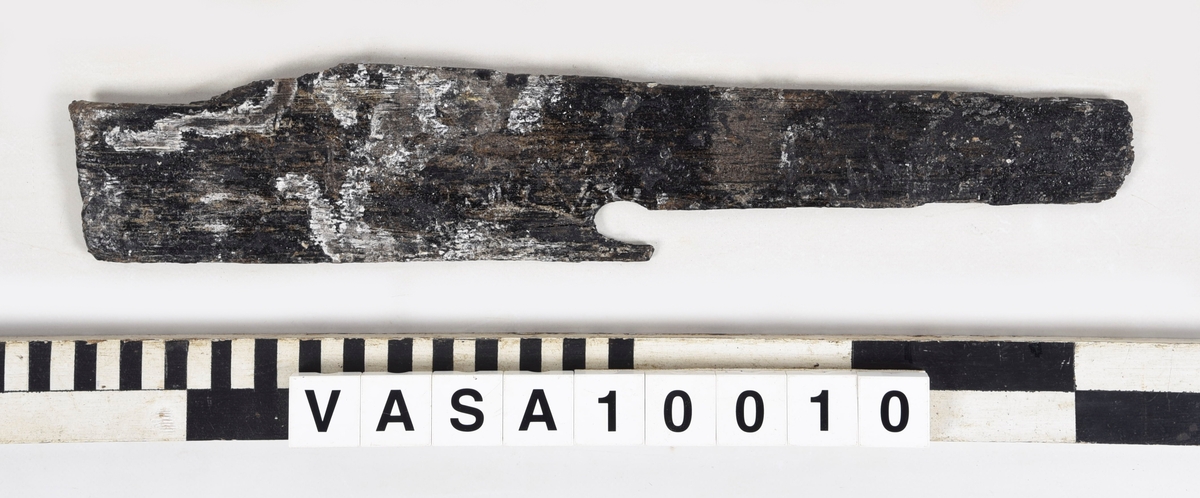 Fragment, med del av fasad kant. Ett vinklat hörn.
Mycket vittrad, smalnar av mot änden. Tjockt lager PEG.