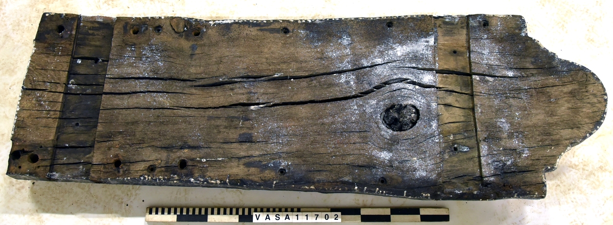 Lavettbotten, flertal sprickor med splitter, stor trä knut i mitten.

För mer information se Dokumentationsblankett under Referenser – Länkade filer.

Text in english:
Heavely cracked split gun-bed, large central knot.

For more information see the Documentation form under References – Linked files.