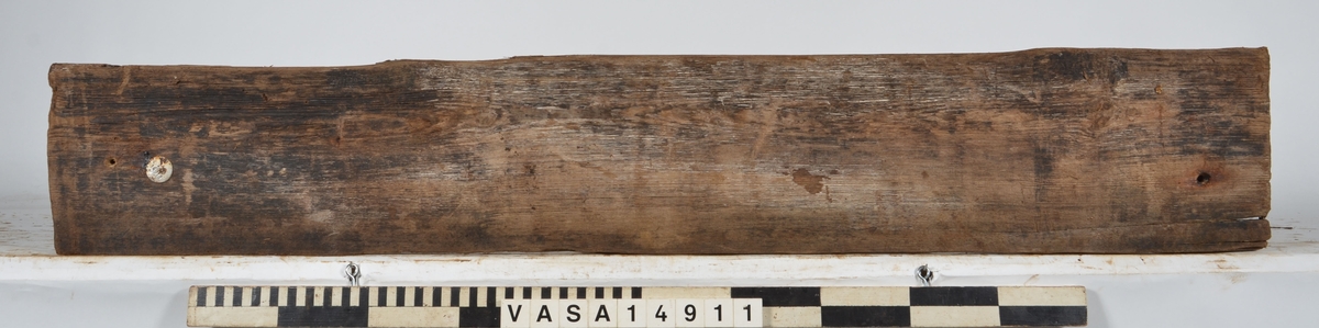 Bräda som tillhör alpumpkistan i hålskeppet. Stor längsgående spricka vilken separerar detta föremål från 14734. En del skador på kanterna.