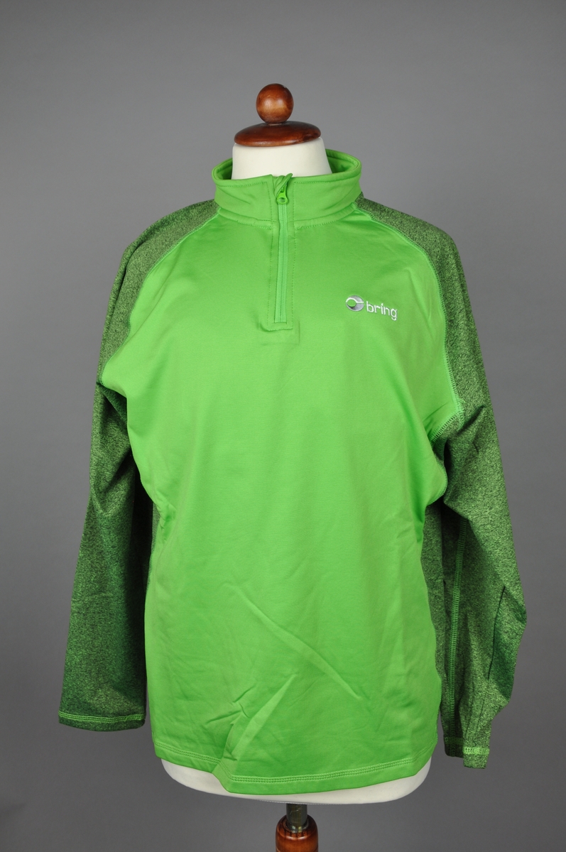Grønn langermet genser i micropolyester med børstet innside. Glidelås ved halsåpningen. Genseren er i størrelse "Medium". Plagget har en melert mørkegrønn tone på ermer og sidene. Et brodert logomerke på fremsiden.