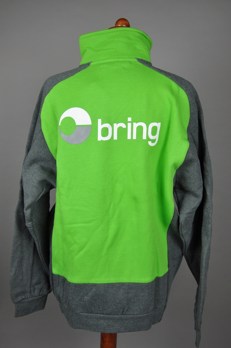 Grønn og gråmelert jakke i bomull 80 % og polyester 20%. Brings logo på ryggen og et lite brodert logomerke på venstre bryst. Jakken er størrelse "Medium" og har glidelås i front. To store sidelommer med glidelås.