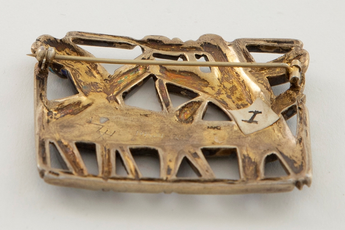 Tilnærmet kvadratisk brosje i forgylt sølv, dekorert med grubeemalje. Gjennombrutt overflate som danner stiliserte dyreskikkelser. Nål festet til baksiden.