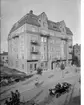 Femvånings bostadshus med affärer i gatuplanet.
Bröderna Lundholm, läder och skodon i parti.
En öppen automobil på gatan. 
Bilen som ses på gatan är en Hupmobile Modell 32, en bilmodell som tillverkades 1912-1915. Den ägdes av godsägare Pontus Burén och fick den 29:e februari 1916 registreringsnummer T40.