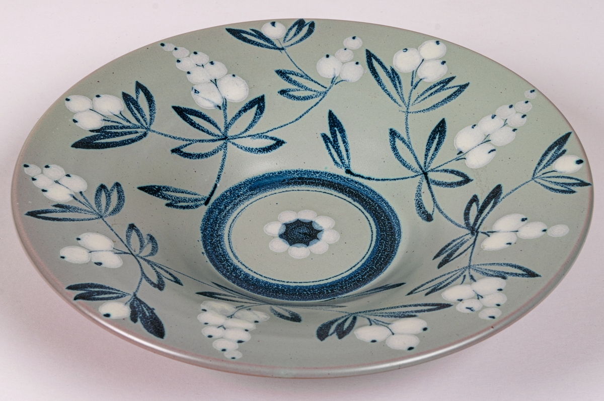 Handmålad skål i modell 4308 med dekor BV; med blå och vita bärkvistar på duvblå botten, blå rand i botten. Formgiven av konstnär Eva Jancke-Björk 1934.
