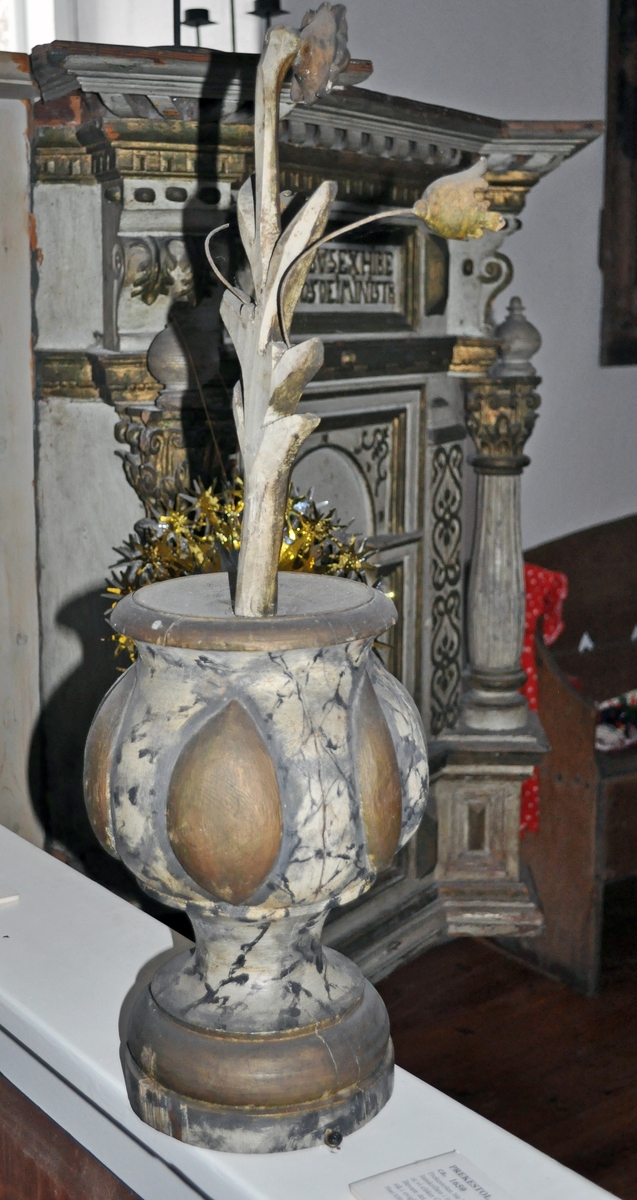 Fra protokollen (Hoel):
Trevase med fritstaaende blomsterprydelser, enten fra prækestolhimlen eller fra korrekkverket i Solum kirke.
