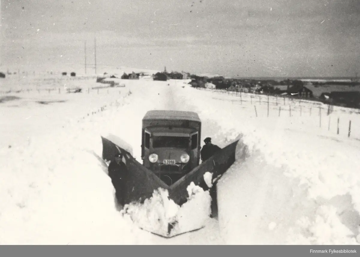 A/S Polarbil sin Y-2096 brøyter i Nyborgveien i Vadsø, ca. 1940. Her ser man brøytebilen står i ro. En mann står bak plogen. I bakgrunnen ser man Vadsø. Se også bildene 577-588.