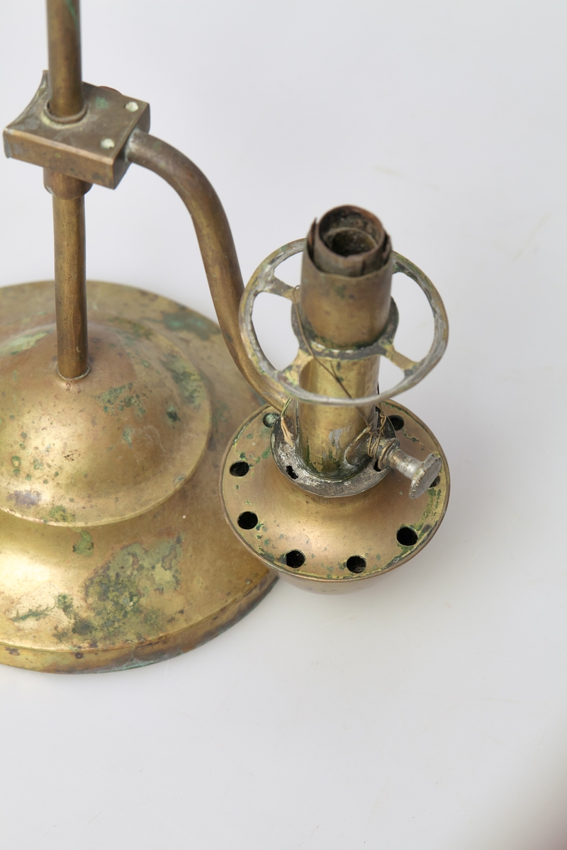 Bordlampe av messing med innhul fot. I foten står en stang med bærehempe i toppen. Oljebeholder og lampe sitter på hver sin side av stangen, og er festet til denne med en glideanordning som kan skrues fast i ønskelig høyde. Lampeglasset er borte.