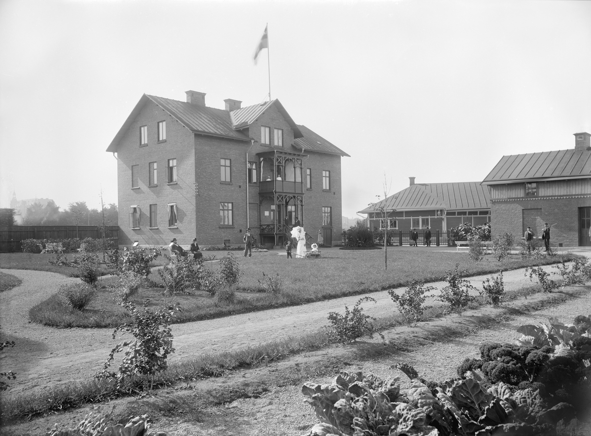 År 1897 startades Linköpings nya gasverk i stadens norra utkant. Det tidigare gasverket låg opassande centralt på Sankt Larsgatan. Bilden visar kontorsbyggnaden i hörnet av dåvarande Bangårdsgatan och Fabriksgatan. På grusgången står gasverksingenjören Gustaf Corlin invid hustru och barn.