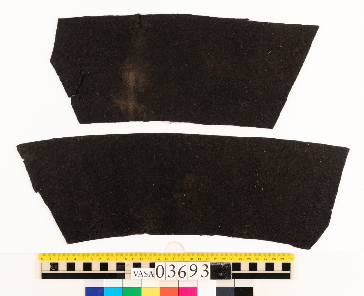 Textil.
2 tillskurna bitar av mörkbrun tät, hård filt. Små runda hål syns på ett flertal ställen på fragmenten, troligen från olika sömmar.

Textildokumentation 2018:

Ingår i kontextgrupp: ÖB31
Fyndnumret 03693 innehåller 2 fragment (ÖB31.5:1-2). Fyndnumret innehåller även ett tråd.
Fragmenten är av filtad ull i mycket fin kvalitet och med en tät filtning. Fragmenten är tillskurna. Det finns tydliga märken efter stygn och stygnhål utefter kanterna. Ca 10 st runda hål, möjligen stansade.
På ena sidan av båda delarna finns snedställda avtryck som liknar avtryck från snedställda pikéringsstygn. Delarna är tillskurna och har jack utefter kanterna som skulle kunna vara passmärken. Spår av kastsöm på delar av kanterna.
Materialet är stelt som om det skulle kunna vara behandlat med något. Ingen tydlig lukt.
Delarnas ena sida har en slätare struktur. 
ÖB31.5:2. På tvären finns spår av ett veck. Vid vecket ett blekt område. Utefter kanter bristningar. 
Det finns små tryckmärken alt. märken av skadeddjur.

Tråden är tunn och vågig, möjlig del av tjockare tråd. 

TEKNIK Typ.nr: ÖB31.5:1-2
Fibermaterial: ull
Garngrovlek (mm): 0,7-0,9
Färg: mycket mörk, möjlig svart

TEKNIK Typ.nr: (ÖB31.5:1-2) tråd:
Antal tråd: 1
Fibermaterial: ull
Spinnriktning: z
Färg: svart

Dokumenterad av AS nov 2017, maj 2018.
Införd av MS juli 2018.