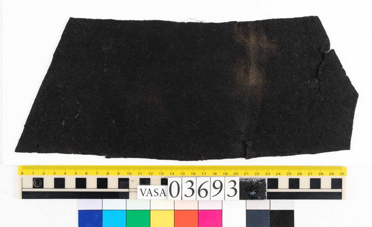 Textil.
2 tillskurna bitar av mörkbrun tät, hård filt. Små runda hål syns på ett flertal ställen på fragmenten, troligen från olika sömmar.

Textildokumentation 2018:

Ingår i kontextgrupp: ÖB31
Fyndnumret 03693 innehåller 2 fragment (ÖB31.5:1-2). Fyndnumret innehåller även ett tråd.
Fragmenten är av filtad ull i mycket fin kvalitet och med en tät filtning. Fragmenten är tillskurna. Det finns tydliga märken efter stygn och stygnhål utefter kanterna. Ca 10 st runda hål, möjligen stansade.
På ena sidan av båda delarna finns snedställda avtryck som liknar avtryck från snedställda pikéringsstygn. Delarna är tillskurna och har jack utefter kanterna som skulle kunna vara passmärken. Spår av kastsöm på delar av kanterna.
Materialet är stelt som om det skulle kunna vara behandlat med något. Ingen tydlig lukt.
Delarnas ena sida har en slätare struktur. 
ÖB31.5:2. På tvären finns spår av ett veck. Vid vecket ett blekt område. Utefter kanter bristningar. 
Det finns små tryckmärken alt. märken av skadeddjur.

Tråden är tunn och vågig, möjlig del av tjockare tråd. 

TEKNIK Typ.nr: ÖB31.5:1-2
Fibermaterial: ull
Garngrovlek (mm): 0,7-0,9
Färg: mycket mörk, möjlig svart

TEKNIK Typ.nr: (ÖB31.5:1-2) tråd:
Antal tråd: 1
Fibermaterial: ull
Spinnriktning: z
Färg: svart

Dokumenterad av AS nov 2017, maj 2018.
Införd av MS juli 2018.