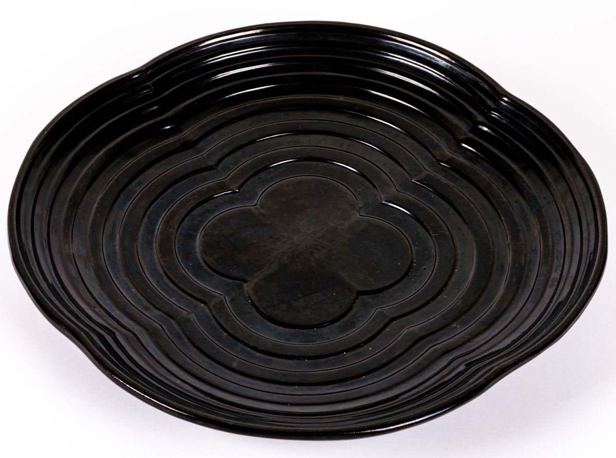 Stort svartglaserat fat, kallat "fyrklöverfat", av lergods, av Ewald Dahlskog, Bo Fajans. Modell D1.