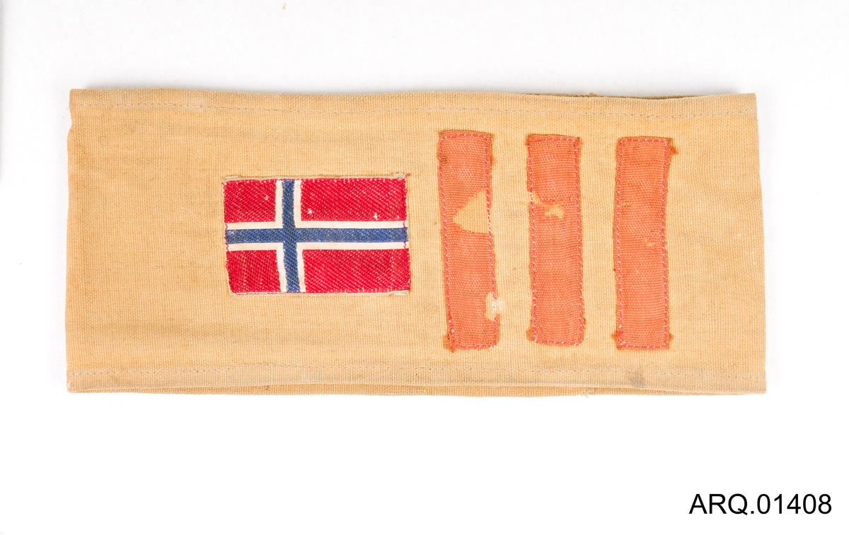 Armbind i seildukstoff, lysegult med påsydd norsk flagg og 3 røde striper.