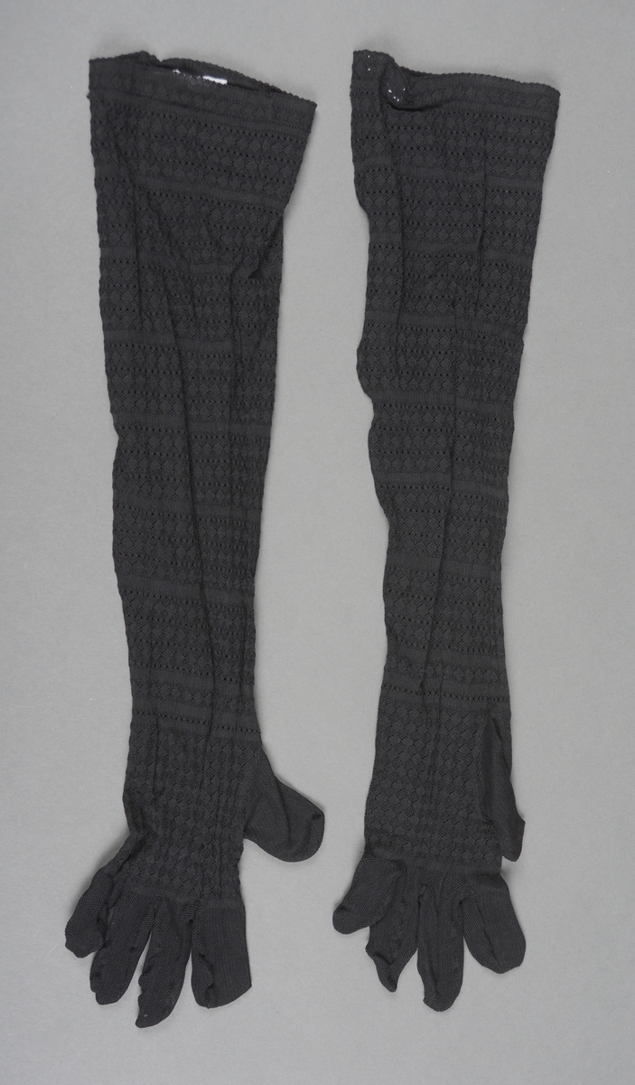 Et par lange hansker sydd av svart silketrikot. Hånd og arm har mønsterstrikk (hullmønster, ruter og striper) i gjentagende mønster. Fingrene er av et elastisk nettingstoff (derfor ser fingrene veldig korte ut).