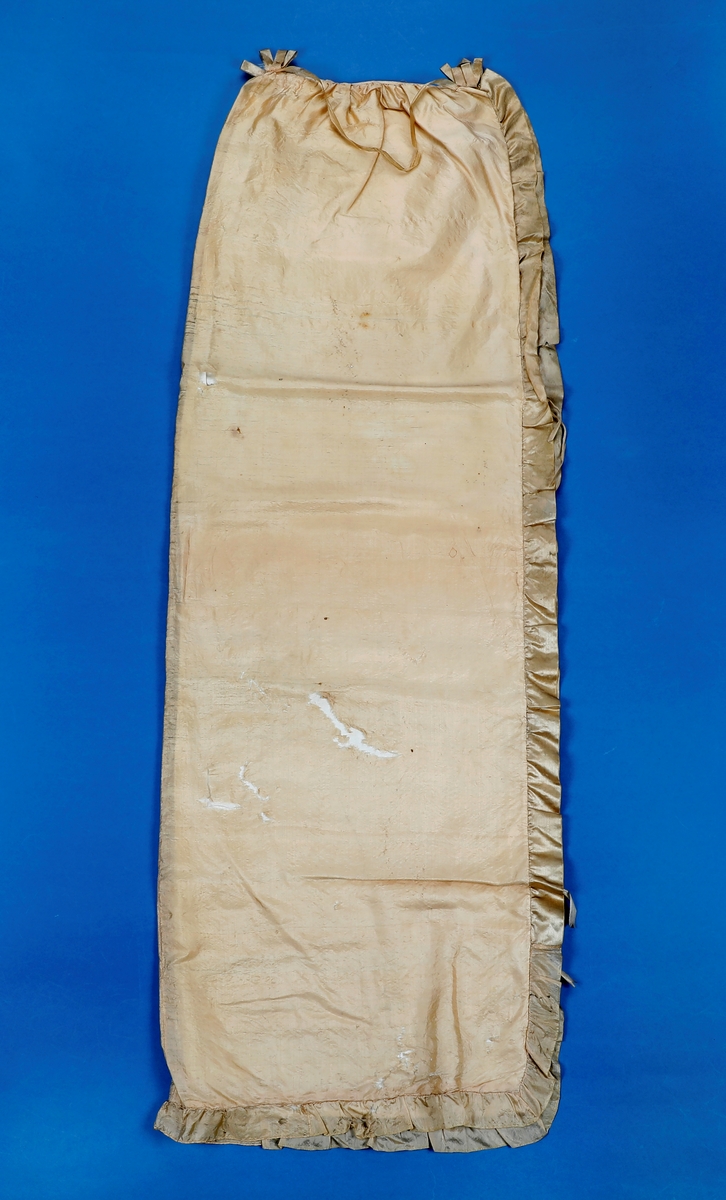 Dåpskåpe i tynn silke med rysjekappe langs alle sidene. På hodet er stoffene rynket sammen og det er laget en rosett av silkebånd foran og bak med silkebånd imellom. Kåpen er fore med bomullslerret. Det er festet silkebånd til knyting på fire steder på hver side av kåpen.Silken er skjør og hullete.