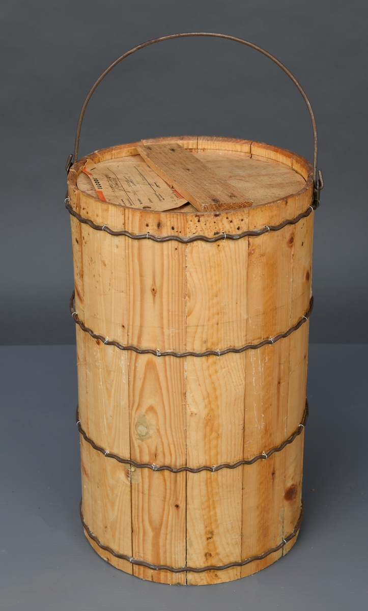 En dall med lokk av ubehandlet tre. Dallen er lagget og holdes sammen med fire bølgete metallbånd. Båndene er festet med små metallringer i dallen. Oppe er det en hank festet i hver side med metallfester. Dallen har et rundt trelokk. Lokket består av to halvsirkler som holdes sammen ved at et tverrstykke er spikret på. På lokket er det stiftet på en lapp med informasjon om transport.