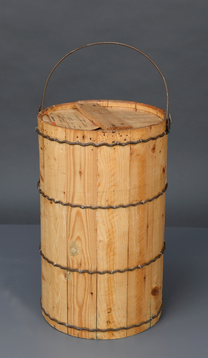 En dall med lokk av ubehandlet tre. Dallen er lagget og holdes sammen med fire bølgete metallbånd. Båndene er festet med små metallringer i dallen. Oppe er det en hank festet i hver side med metallfester. Dallen har et rundt trelokk. Lokket består av to halvsirkler som holdes sammen ved at et tverrstykke er spikret på. På lokket er det stiftet på en lapp med informasjon om transport.