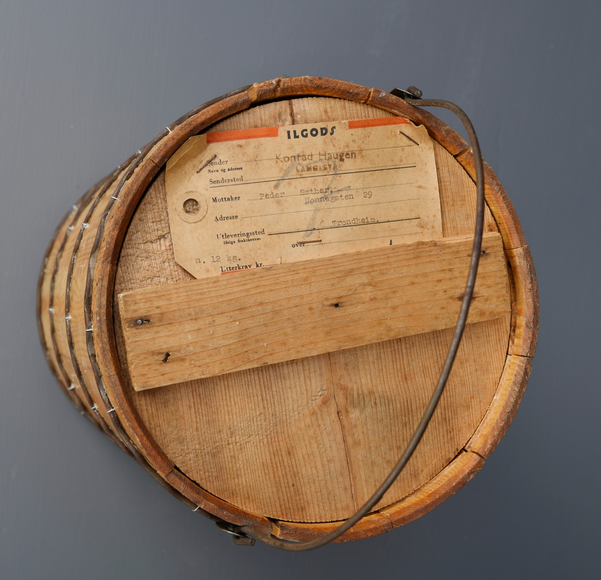 En dall med lokk av ubehandlet tre. Dallen er lagget og holdes sammen med fire bølgete metallbånd. Båndene er festet med små metallringer i dallen. Oppe er det en hank festet i hver side med metallfester. Dallen har et rundt trelokk. Lokket består av to halvsirkler som holdes sammen ved at et tverrstykke er spikret på. På lokket er det stiftet på en lapp med informasjon om transport.