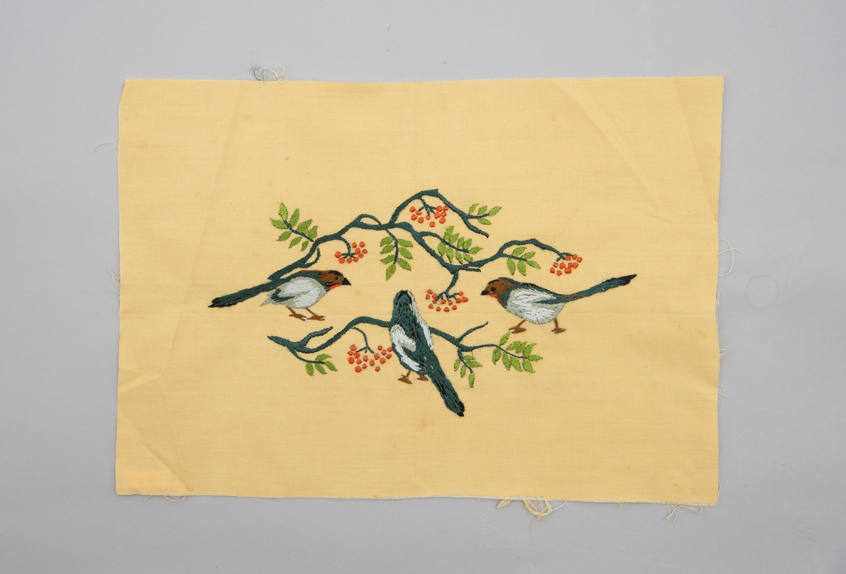 Brodert veggbilde med fuglemotiv. Tre fugler og to greiner med rognebær.