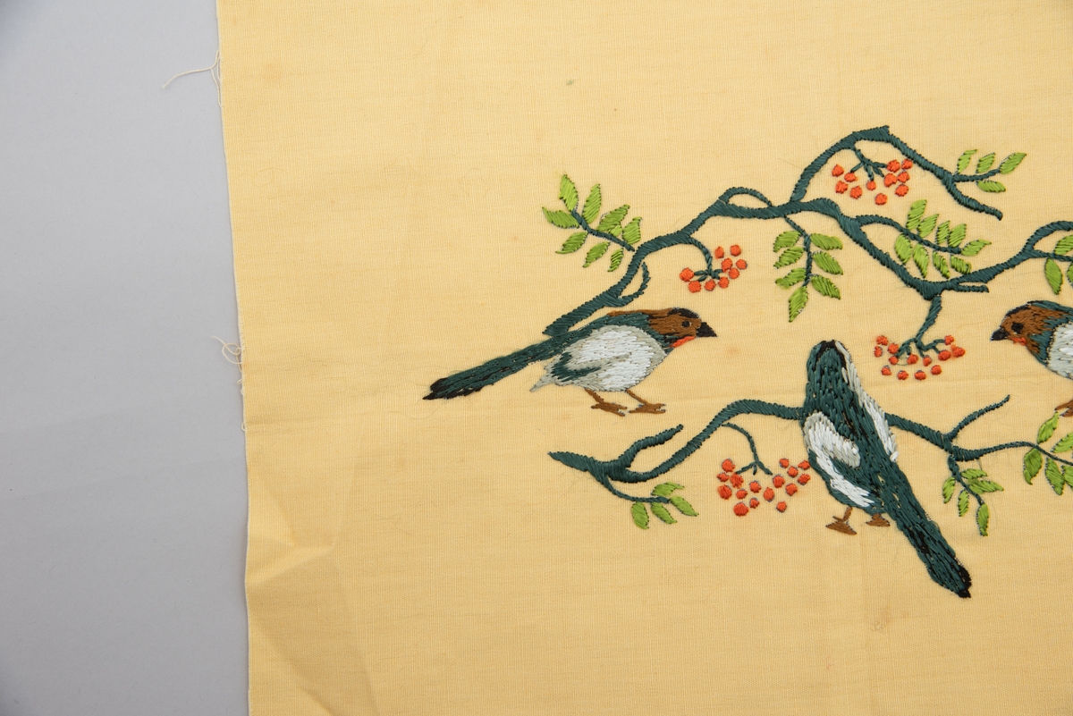 Brodert veggbilde med fuglemotiv. Tre fugler og to greiner med rognebær.