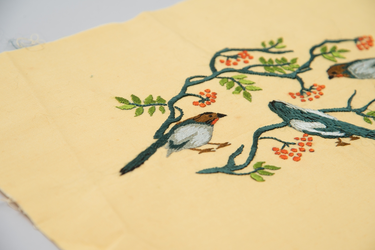 Brodert veggbilde med fuglemotiv. Tre fugler og to greiner med rognebær.