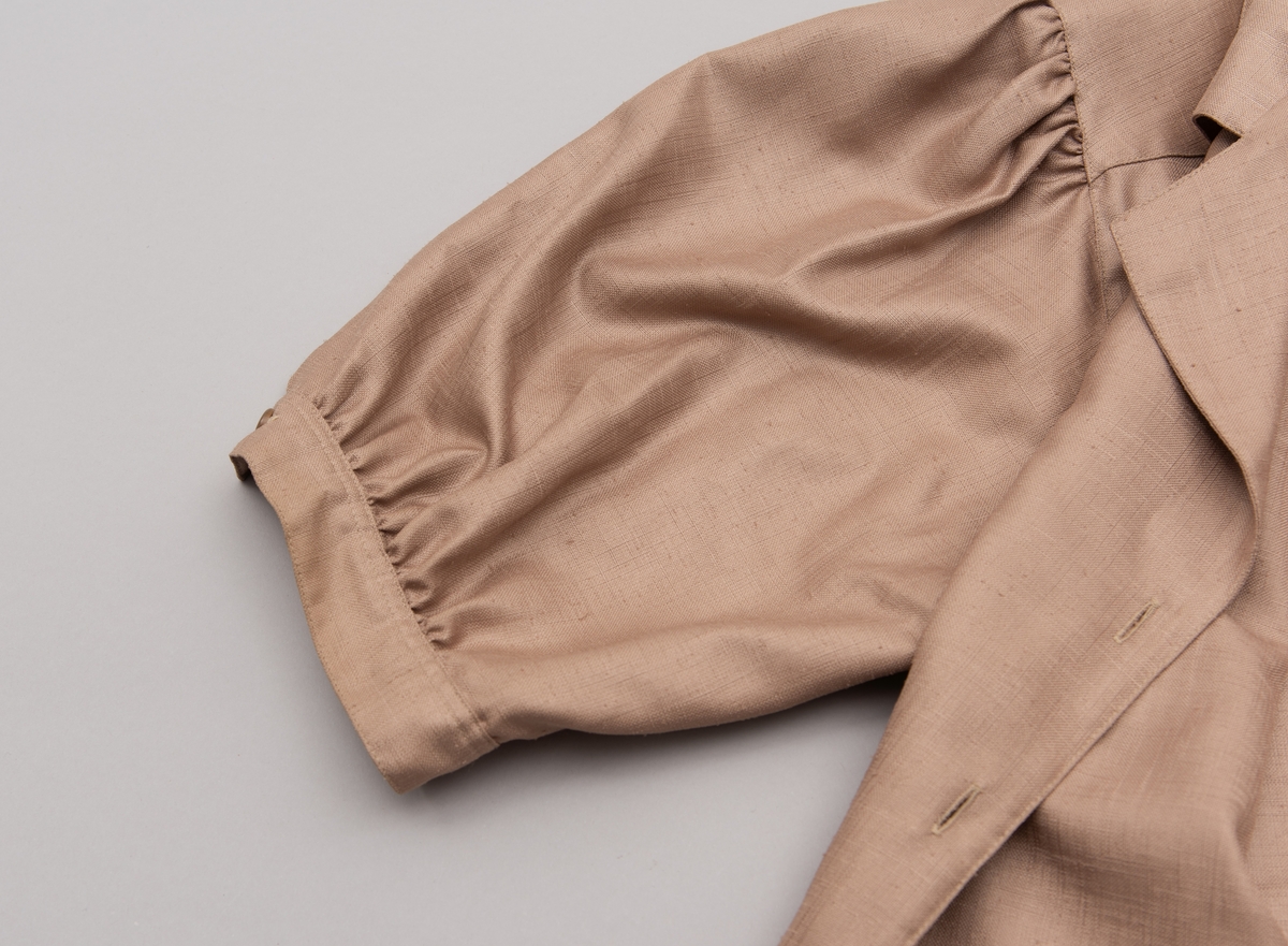 En grå-beige draktkjole og to tynne fargede sjal. Drakta er tredelt med bluse, skjørt og jakke. Drakt og sjal ble brukt sammen.