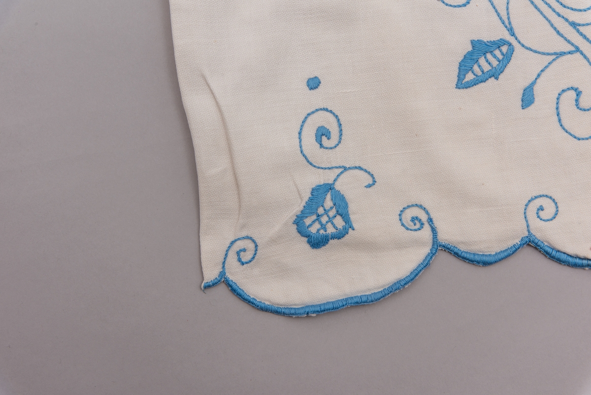 Hvit tekstilpose med blått broderi. Det er dusker på enden av tråden.