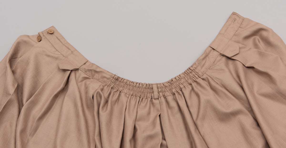 En grå-beige draktkjole og to tynne fargede sjal. Drakta er tredelt med bluse, skjørt og jakke. Drakt og sjal ble brukt sammen.