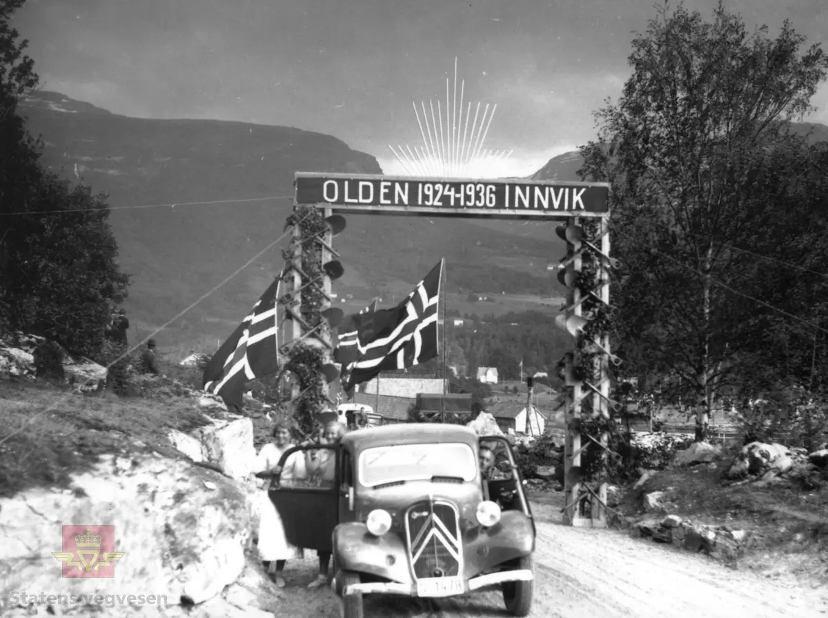 Offisiell opning av "Singervegen" mellom Innvik og Olden 23. juni 1936 og Hans Majestet Kong Haakon VII var med på opninga. 

Vegen ble bygd i åra 1924 - 1936 og blei kalla "Singervegen" fordi den amerikanske millionæren William H. Singer forskorterte halvparten av kostnadane på veganlegget med kr. 450 000,-.

I anledninga var det i Innvik reist ein æresport dekorert med arbeidsreiskap, - hakker, spader, meislar og minebor.

(Informant/kjelde: Per Birger Lomheim, pensjonert tilsett i Statens vegvesen i Sogn og Fjordane og nettstaden "Kulturhistorisk leksikon", artikkelen "Singersteinen på Hildeneset i Innvik" av Hermund Kleppa.)

Framføre æresporten står en Citröen Traction Avant med kjenneteikn S-1478.
