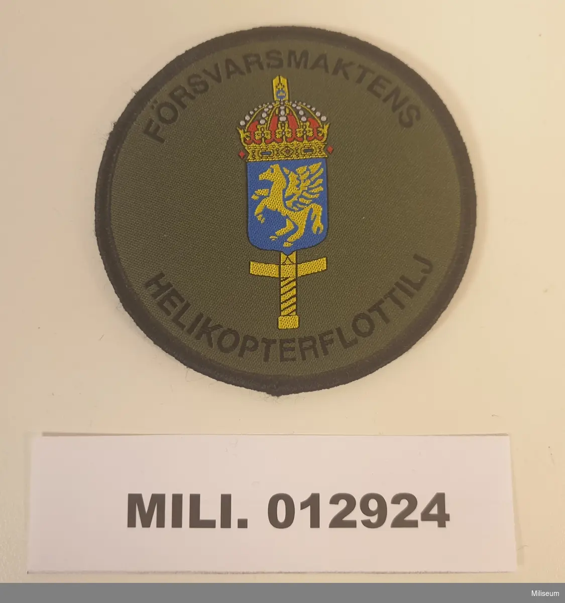 Tilläggstecken med maskinvävt motiv. Med kardborrefästning på baksidan. Att fästas på fältuniformens vänstra överärm.