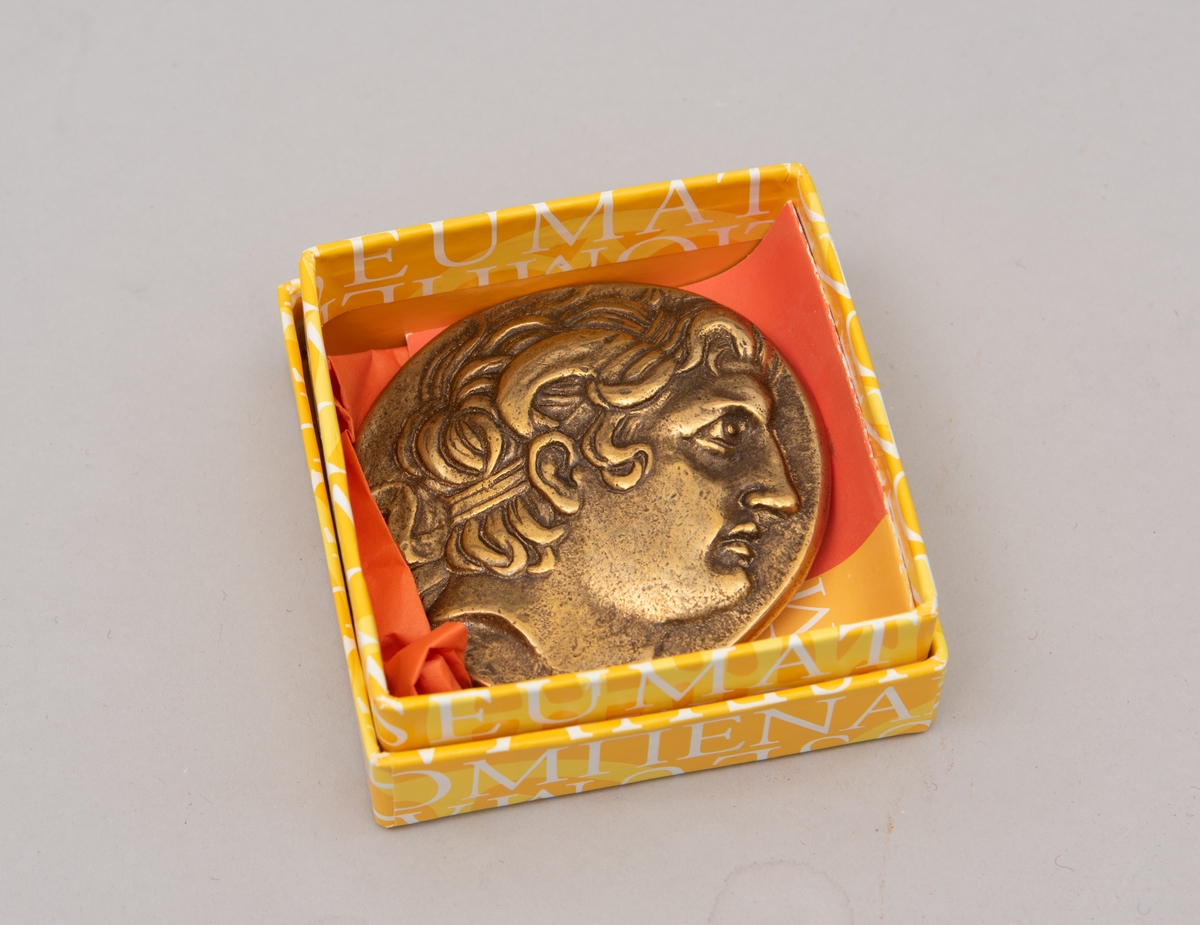 Brevpresse i bronse, med eske og informasjonsfolder. Motiv (baksiden) av gudinnen Athene på tronen som holder Nike. På forsiden portrett av Aleksander den store. Brevpressen er fra museumsbutikken til Benaki Museum i Athen. På informasjonstekst i esken står: Bronze replica. Gold stater of Lysimachous of Thrace (306-281 BC).