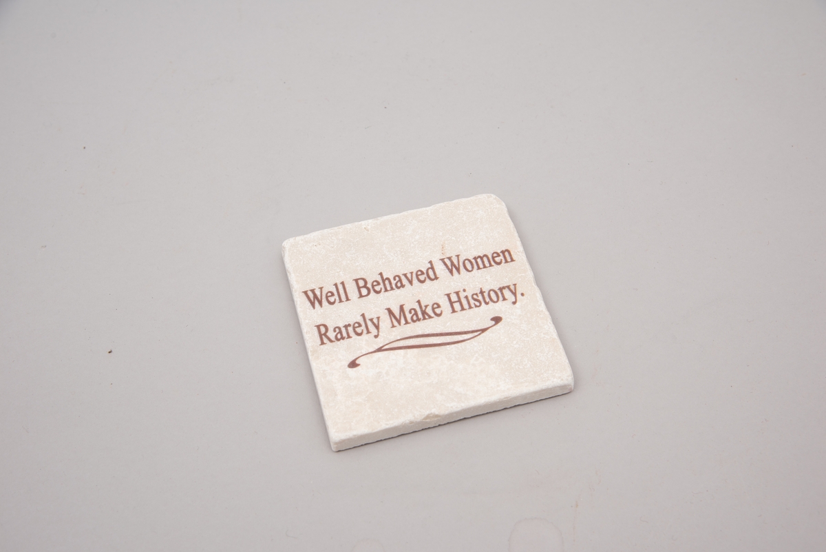 Marmorflis og souvenir fra Newsport Mansions med påført slagord "Well Behaved Women Rarely Make History". Tilhørende eske og informasjonsfolder. Mottoet påført marmorflisa er i ettertida blitt brukt til å beskrive Alva Vanderbilt Belmont (1853-1933) og andre kvinner som kjempet for kvinners stemmerett på begynnelsen av 1900-tallet i USA under slagordet "Votes for Women". Selve "Votes for Women"-mottoet ble brukt i 1909 på et berømt "open house" stemmerettsmøte holdt på Marble House, Newport, Rhode Island".