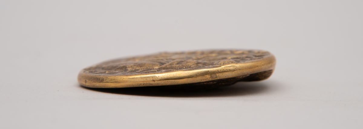 Brevpresse i bronse, med eske og informasjonsfolder. Motiv (baksiden) av gudinnen Athene på tronen som holder Nike. På forsiden portrett av Aleksander den store. Brevpressen er fra museumsbutikken til Benaki Museum i Athen. På informasjonstekst i esken står: Bronze replica. Gold stater of Lysimachous of Thrace (306-281 BC).