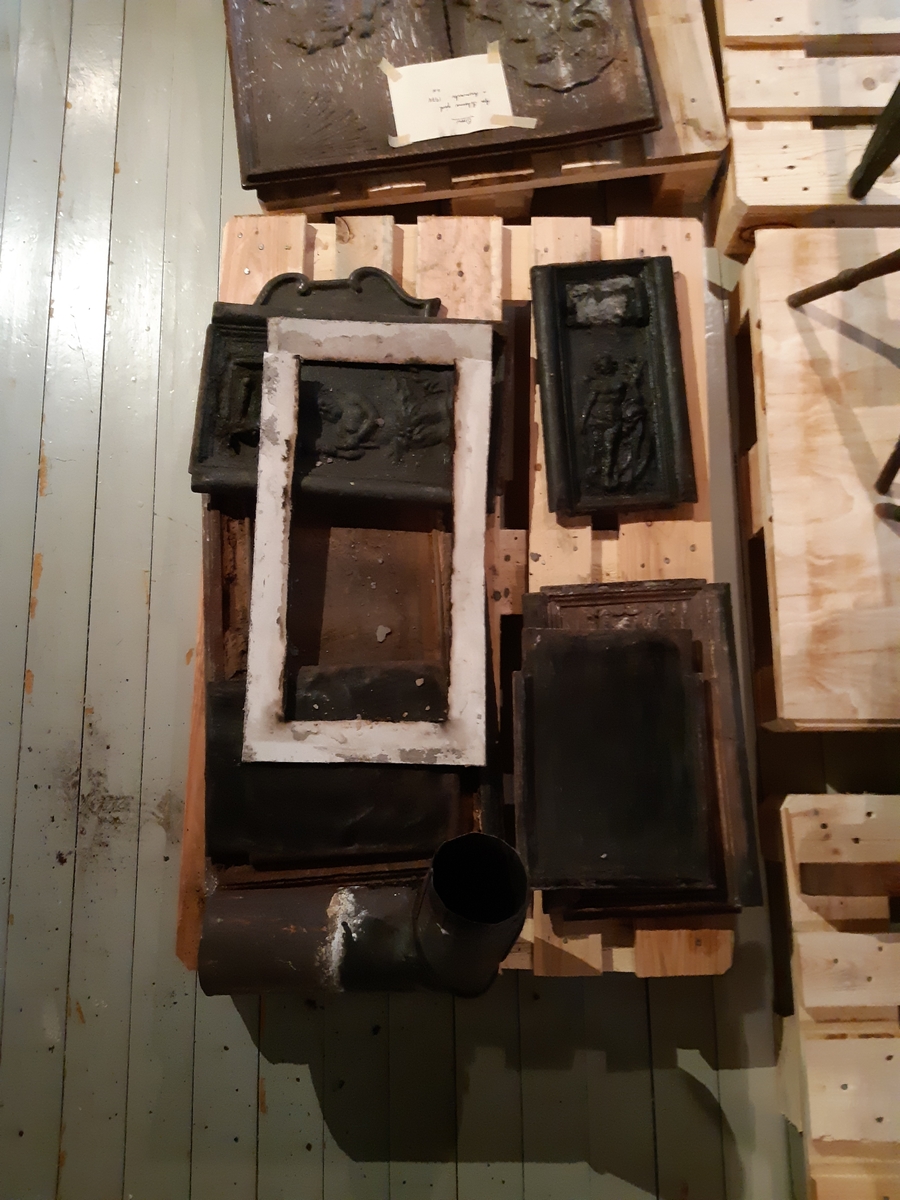 Etasjeovn i støpejern, tre etasjer. Motiv Neptun på fyringskasse. Etasjene med rocailler. Trekrakk, oker farge, kannelerte avsmalnede ben med diamant øverst. 25 deler