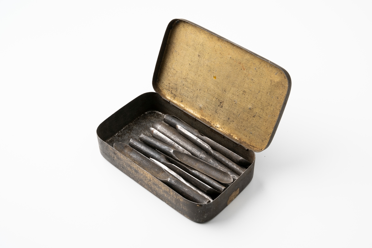 Skedborrar, 21 st, av järn. Ena änden är skålformad, den andra rund. Borrarna förvaras i rektangulär metallask med turkost lock med guldtext: "Kungsblandning".