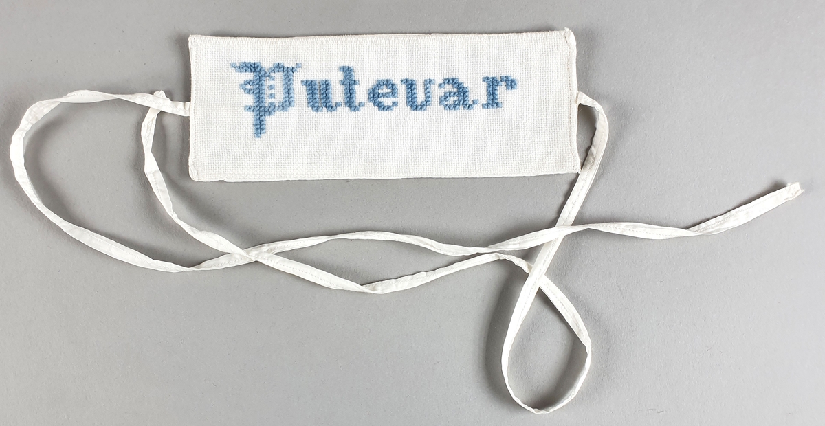To etiketter for lintøy, med broderte bokstaver i rødt og blått. Bånd (snor) festet på midten av hver kortside.