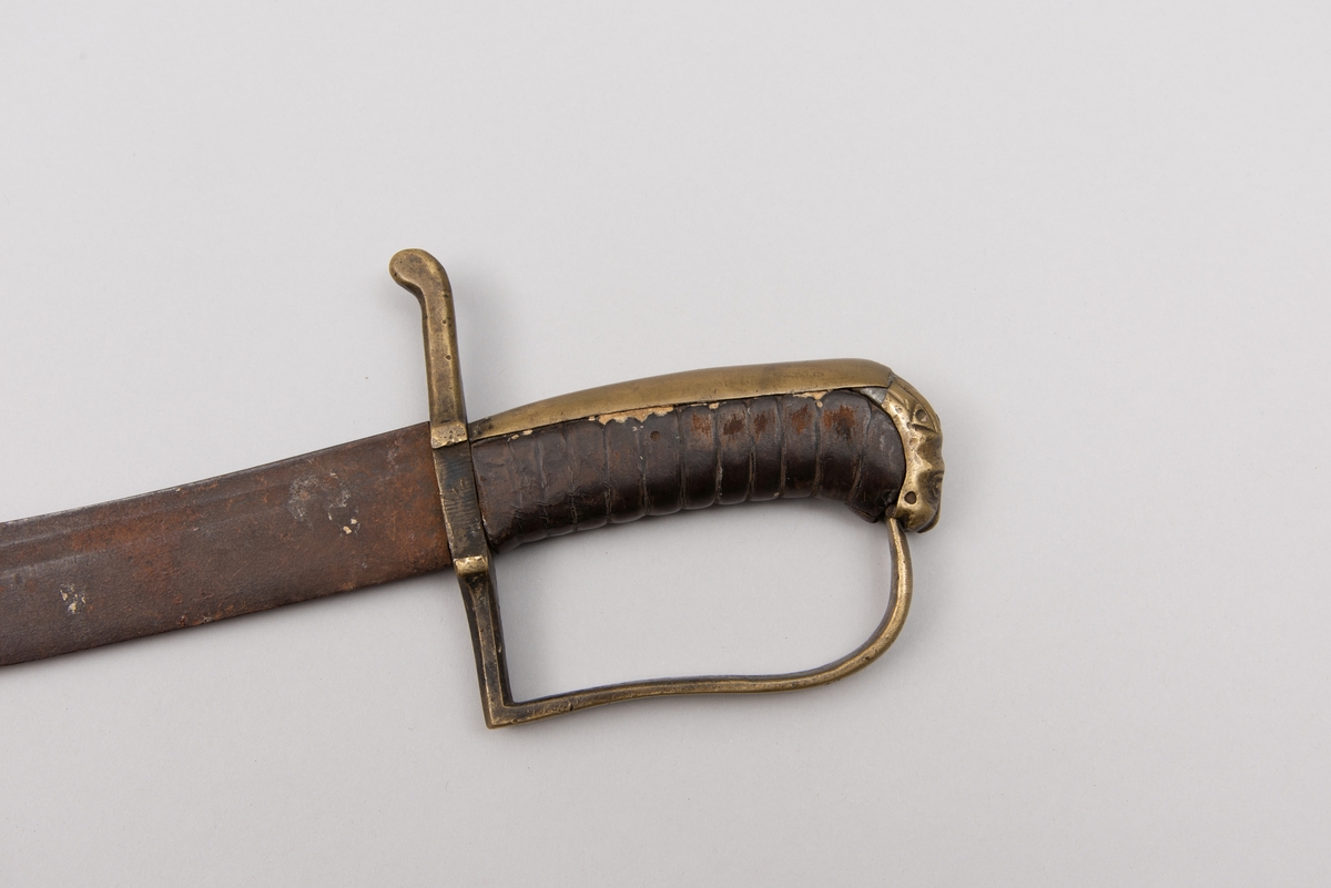 Sabelen er litt krum. Avviket frå rett line gjennom skjefte- aksen er 14.5 cm på 78 cm (mælt frå toppen av skjeftet).Skjeftet har parerstong av messing,ein volutt på den rette toppenden. Under går parerstonga vinkelrett over i ein litt boga vernebøyle opp mot skjeftetoppen av messing, forma som anletsmaske. Grepet er av lær. Klingen av stål har smal blodrand og har utvendig egg.