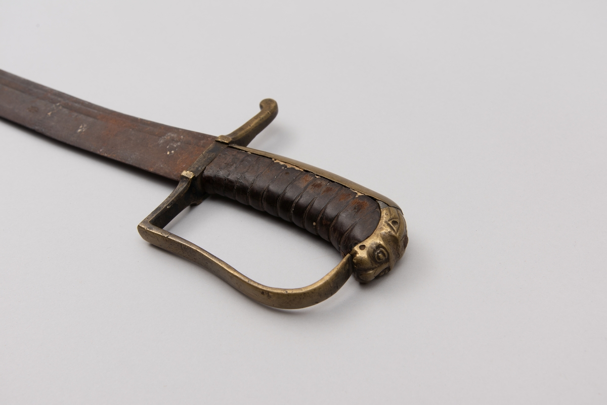 Sabelen er litt krum. Avviket frå rett line gjennom skjefte- aksen er 14.5 cm på 78 cm (mælt frå toppen av skjeftet).Skjeftet har parerstong av messing,ein volutt på den rette toppenden. Under går parerstonga vinkelrett over i ein litt boga vernebøyle opp mot skjeftetoppen av messing, forma som anletsmaske. Grepet er av lær. Klingen av stål har smal blodrand og har utvendig egg.