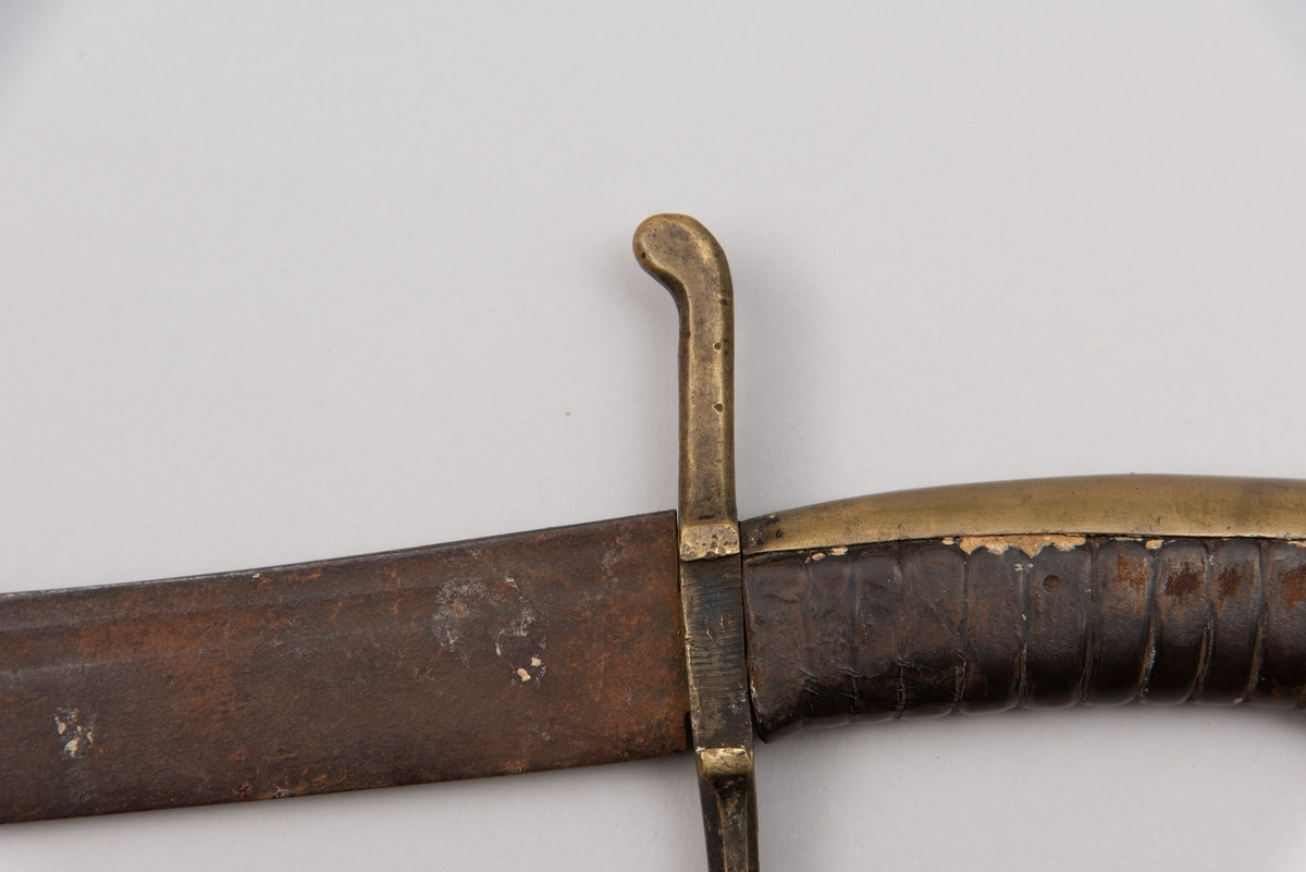 Sabelen er litt krum. Avviket frå rett line gjennom skjefte- aksen er 14.5 cm på 78 cm (mælt frå toppen av skjeftet).Skjeftet har parerstong av messing,ein volutt på den rette toppenden. Under går parerstonga vinkelrett over i ein litt boga vernebøyle opp mot skjeftetoppen av messing, forma som anletsmaske. Grepet er av lær. Klingen av stål har smal blodrand og har utvendig egg.