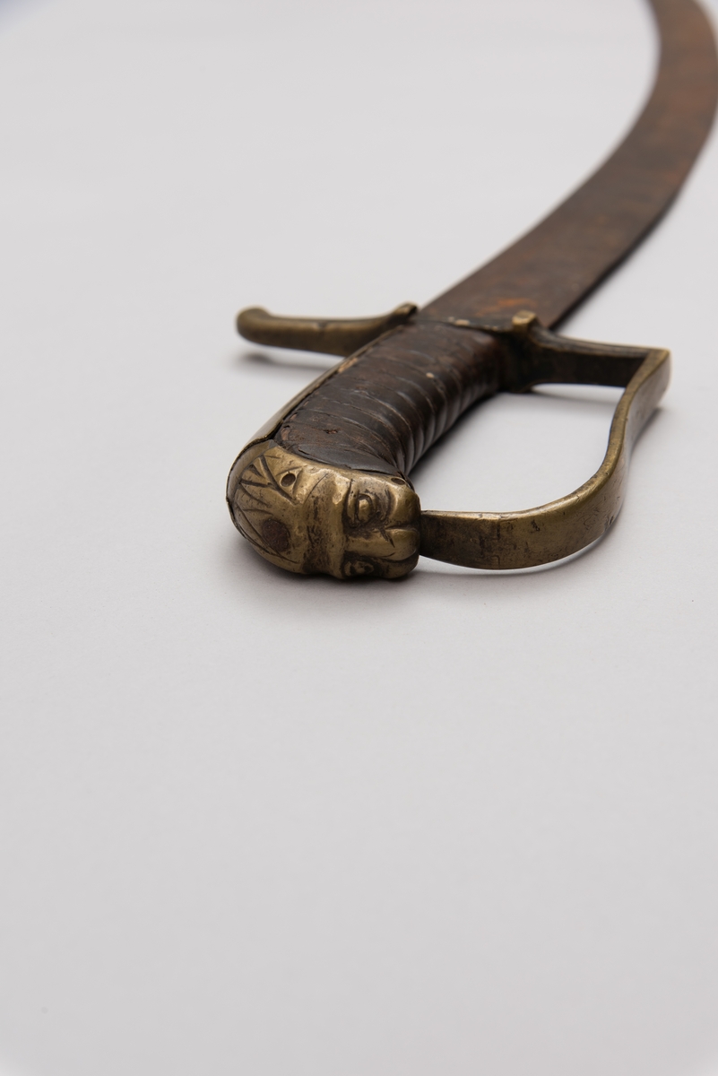 Sabelen er litt krum. Avviket frå rett line gjennom skjefte- aksen er 14.5 cm på 78 cm (mælt frå toppen av skjeftet).Skjeftet har parerstong av messing,ein volutt på den rette toppenden. Under går parerstonga vinkelrett over i ein litt boga vernebøyle opp mot skjeftetoppen av messing, forma som anletsmaske. Grepet er av lær. Klingen av stål har smal blodrand og har utvendig egg.
