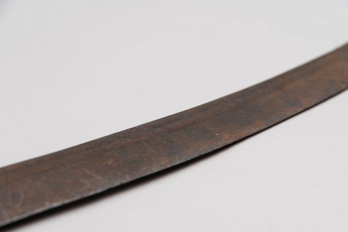 Sabelen er litt krum. Avviket frå rett line gjennom skjefte- aksen er 14.5 cm på 78 cm (mælt frå toppen av skjeftet).Skjeftet har parerstong av messing,ein volutt på den rette toppenden. Under går parerstonga vinkelrett over i ein litt boga vernebøyle opp mot skjeftetoppen av messing, forma som anletsmaske. Grepet er av lær. Klingen av stål har smal blodrand og har utvendig egg.