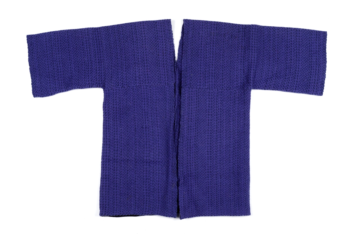 Vams klippet i to deler. Søm i ryggen. Åpen midt foran. Lagt opp med skråbånd i nedkant. Søm over brystet på begge forstykker. Skråbånd er sydd over sømmen på innsiden.