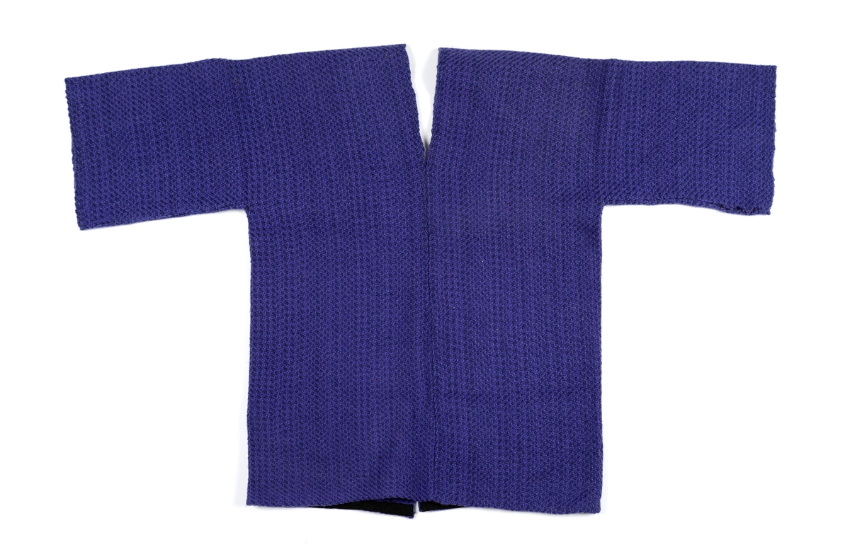 Vams klippet i to deler. Søm i ryggen. Åpen midt foran. Lagt opp med skråbånd i nedkant. Søm over brystet på begge forstykker. Skråbånd er sydd over sømmen på innsiden.