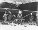 Flygplan FVM J 23 på skidor står i en tälthangar, omkring 1923-26. Fyra militärer vid flygplanet.