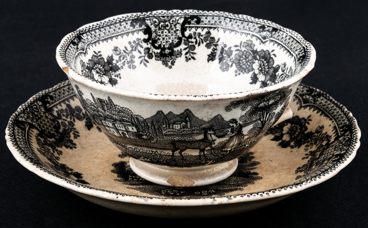 Kaffekopp och fat, med svartvit dekor med landskapsmotiv och blommor. Tillverkad vid Gustavsbergs porslinsfabrik.