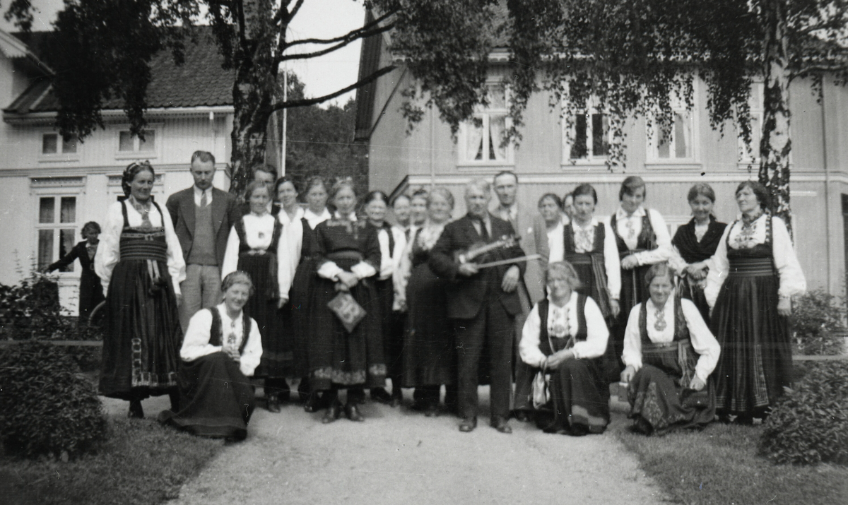 Gruppe med folkedrakter framfor hus