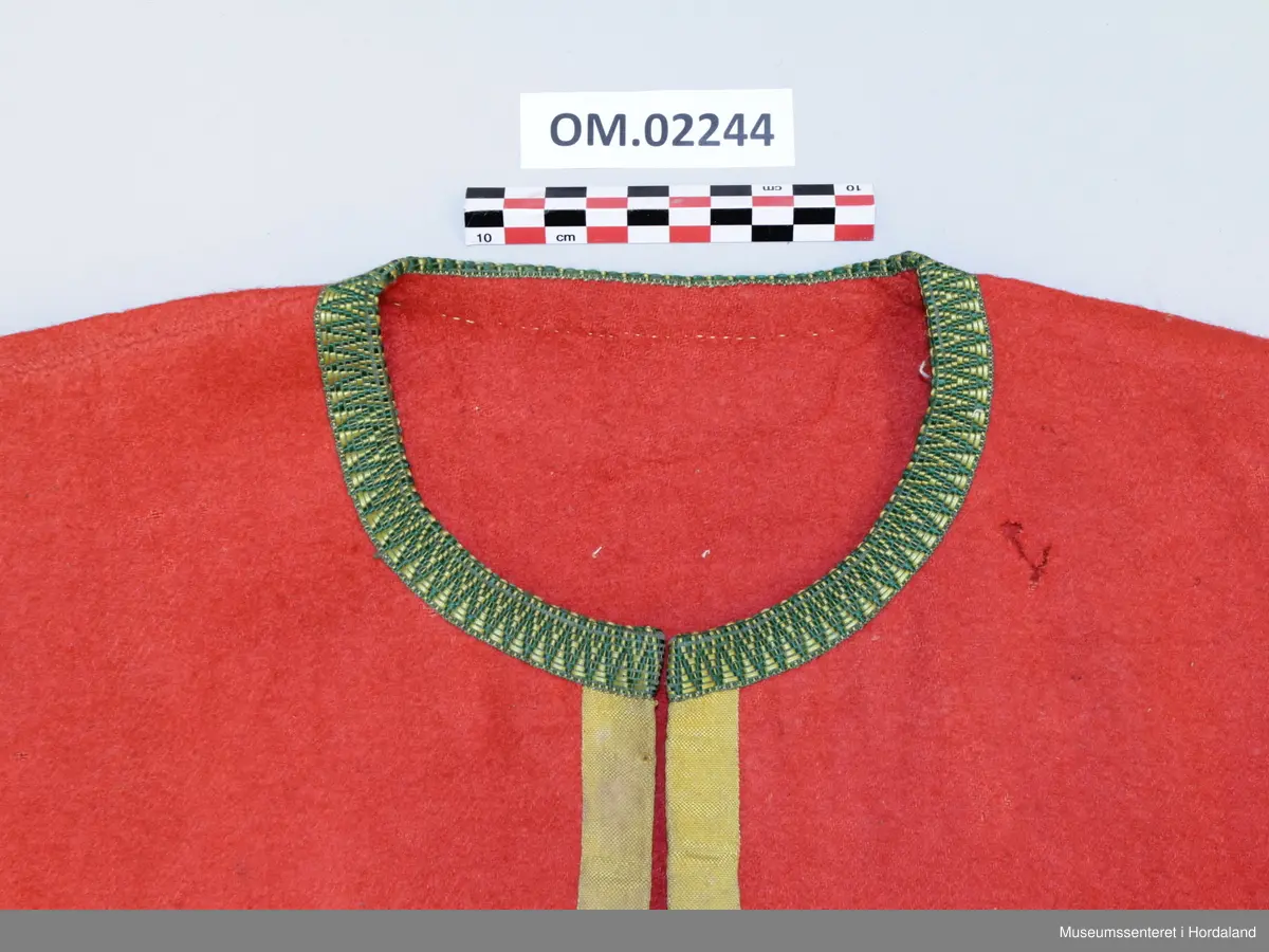 Raudt ull-liv utan fôr. Grøn og gul krokakvarde av silke langs halsopning. Gul silkekvarde langs frontopninga og rundt armhola. Ei hekte under bysten til attlat. Valk rundt kanten nede trekt med lin. I opninga heilt nede er det sydd på snorer av bomullsband (på valken). Livet er reparert nede på venstre framstykke med ein påsydd stoffbit. Handsauma.