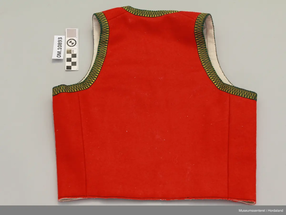 Raudt bunadsliv i ull, med grøn og gul krokakvarding i silke rundt armhola, hals og i front. Ikkje på skuldrar. Fora. Eitt innsnitt på kvart forstykke. Fire hekter til attlat framme.