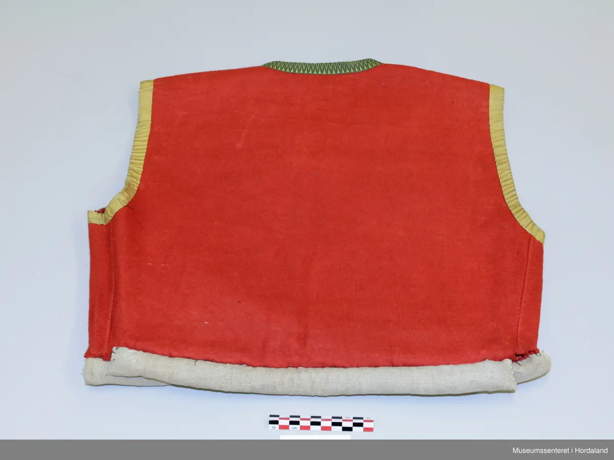 Raudt ull-liv utan fôr. Grøn og gul krokakvarde av silke langs halsopning. Gul silkekvarde langs frontopninga og rundt armhola. Ei hekte under bysten til attlat. Valk rundt kanten nede trekt med lin. I opninga heilt nede er det sydd på snorer av bomullsband (på valken). Livet er reparert nede på venstre framstykke med ein påsydd stoffbit. Handsauma.
